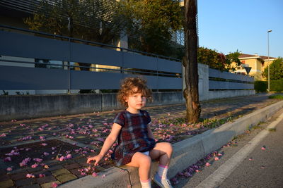 Portrait of girl sitting on curb in city