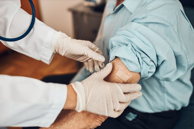 Doctor putting a plaster in place of injection of vaccine to senior man patient