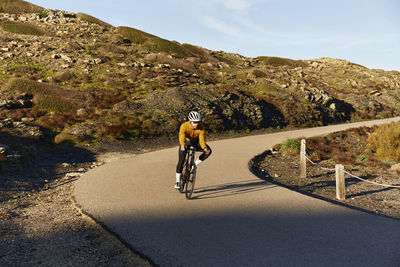 Young cyclist riding cycle in front of rocky mountain on road