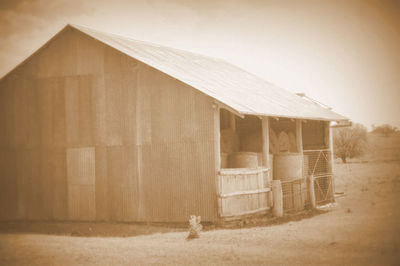 Old barn on field by building against sky