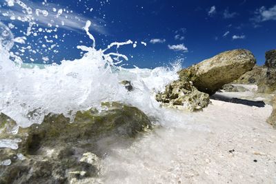 Water splashing on rocks against sky