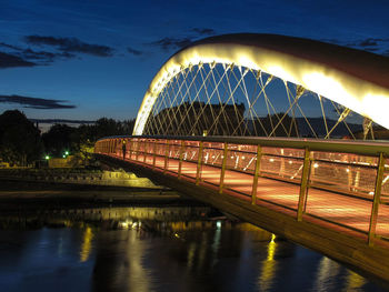 Illuminated bridge over river against sky in city at night