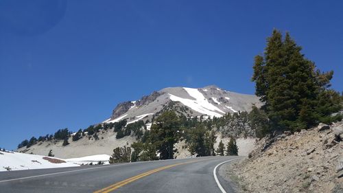 Road amidst snowcapped mountains against clear sky