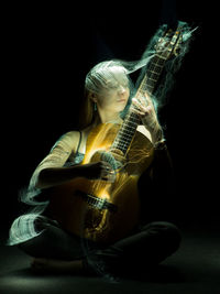 Woman playing guitar against black background