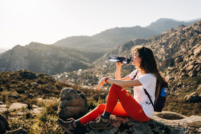 Man sitting on rock looking at mountains against sky