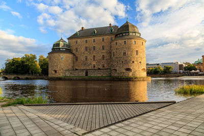 The castle by river against cloudy sky