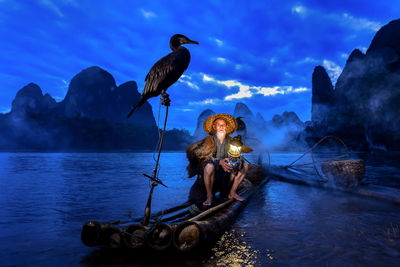 Birds perching on raft by man sitting against sky