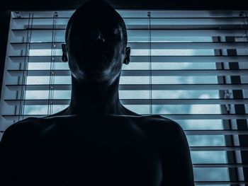 Shirtless man standing against window at home