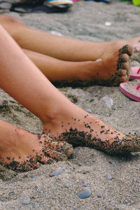 Low section of woman sitting on pebbles at beach