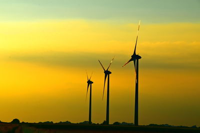 Silhouette wind turbines on field against sky during sunset