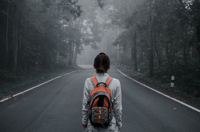 Rear view of woman with backpack standing on road amidst trees in forest