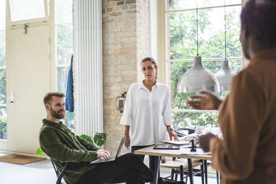 Mid adult woman explaining while male and female entrepreneur sitting at home office