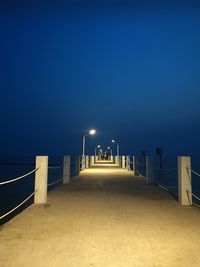 Illuminated walkway against clear blue sky at night