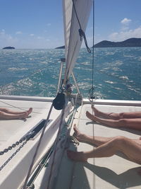 Low section of people relaxing on boat deck over sea against sky