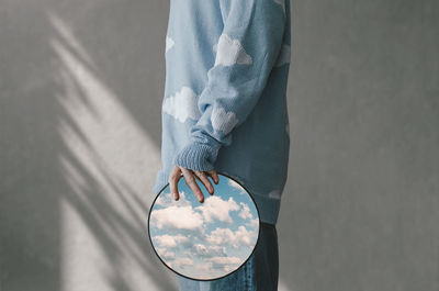 Low section in profile of man holding mirror in which the sky is reflected