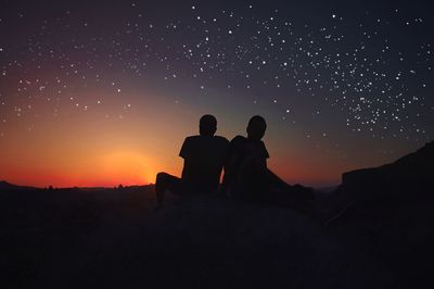 Silhouette men sitting against star field at sunset