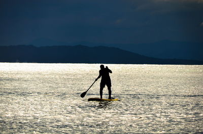 Silhouette man paddleboarding in lake