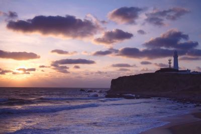 Lighthouse by sea against sky during sunset