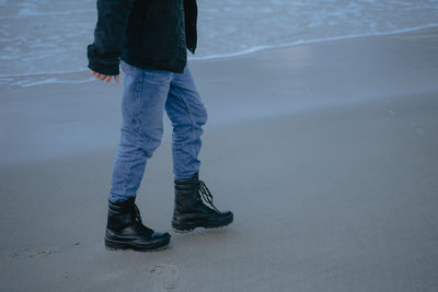 In black massive boots walks along the sandy beach, the lower part of the male body, blue jeans