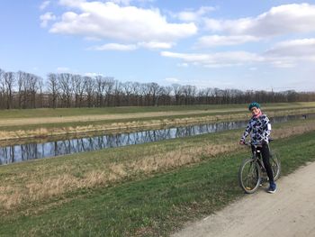 Man riding bicycle on field against sky