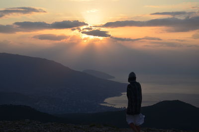 Rear view of woman  standing on mountain against sunset sky