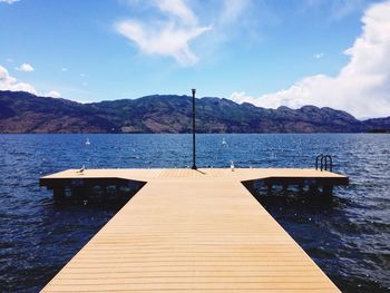 Jetty over river by mountain against sky