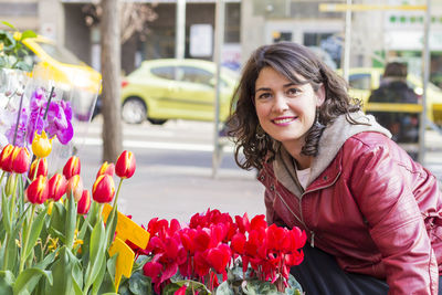 Portrait of smiling mature woman standing by colorful flowers on street