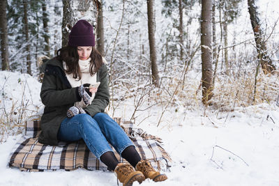 Full length of woman sitting on snow covered land