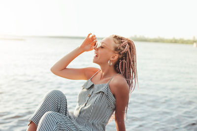 Happy young woman sitting against lake