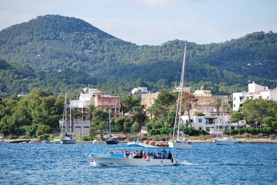 Sailboats in sea by buildings against sky