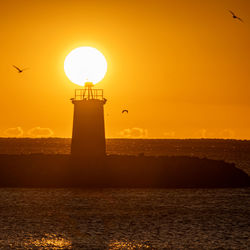 Lighthouse by sea against sky during sunset