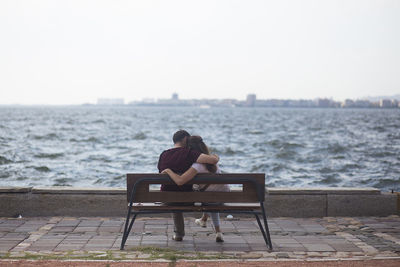  view of couple sitting on bench against sea during sunset