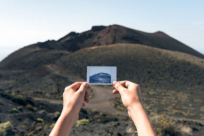 Cropped hands holding photograph against mountain