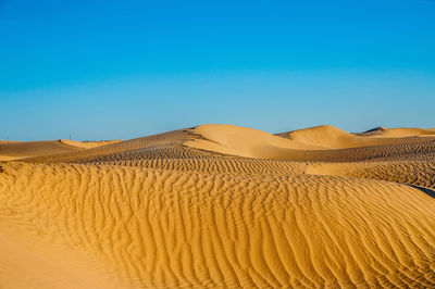 Sand dunes in desert against clear blue sky