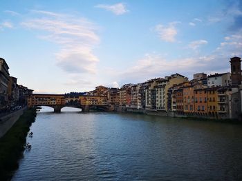 Arch bridge over river amidst buildings in city against sky