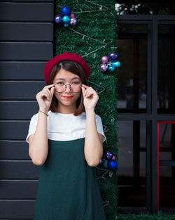 Portrait of smiling young woman standing against window during christmas