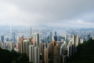 Aerial view of modern city buildings by sea against cloudy sky