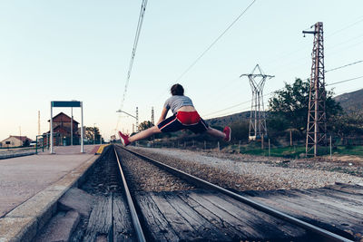 Rear view of man on railroad tracks against clear sky