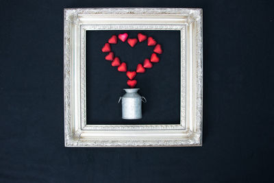 Directly above shot of red heart shapes and canister in picture frame on black background