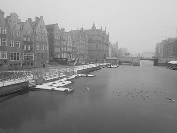 Bridge over river by buildings in city against sky