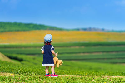Rear view of girl with toy standing on grassy field