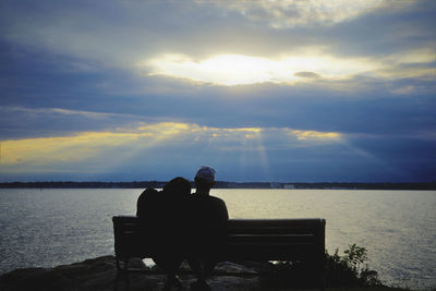 Rear view of silhouette people sitting on bench against sky