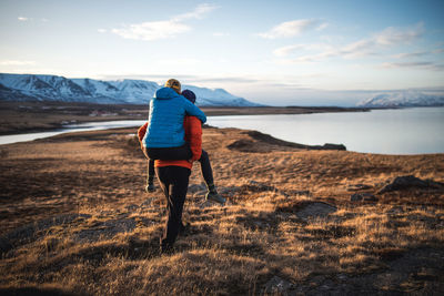 Man carrying woman on piggyback in field with mountains in background