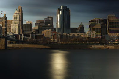 Modern buildings by river against sky in city