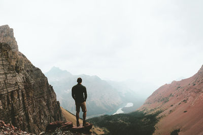 Rear view of man standing on rock amidst mountains at us glacier national park
