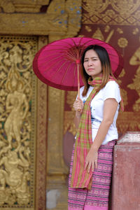 Portrait of woman holding pink umbrella while standing against historic building