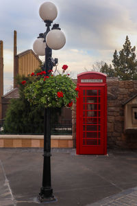 Red telephone booth by street against sky