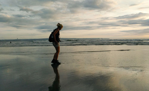 Full length of woman standing on beach against sky during sunset