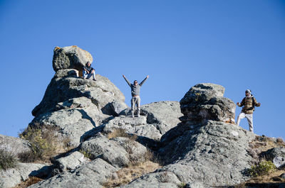 Low angle view of people on rock against clear sky