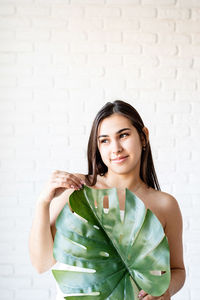  beautiful brunette woman wearing bath towels holding a green monstera leaf in front of her face